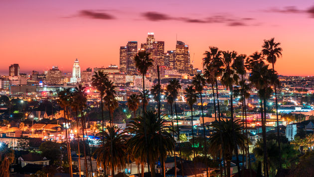 Beautiful sunset of Los Angeles downtown skyline and palm trees in foreground (Photo via choness / iStock / Getty Images Plus)