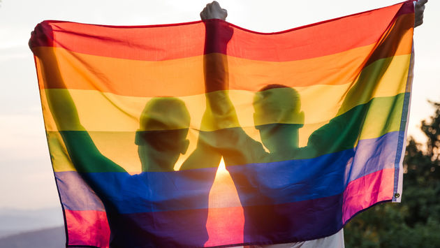 A gay couple holding up a rainbow flag at sunset.