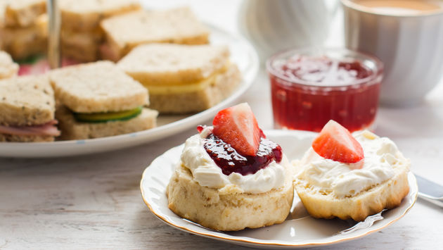 Traditional English afternoon tea: scones with clotted cream and jam, strawberries, with various sandwiches on the background, selective focus. (photo courtesy of Aiselin82 /iStock / Getty Images Plus)
