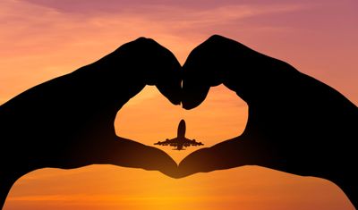 Silhouette of heart-shaped hands around an airplane at sunset