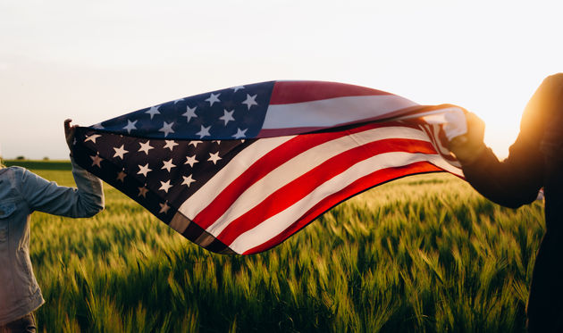 Hands holding American flag in a wheat field on Independence Day.