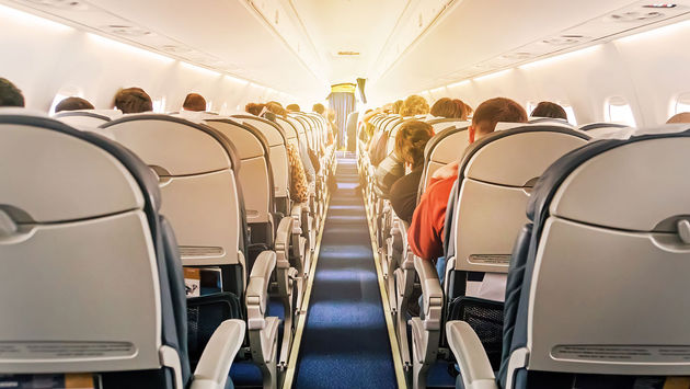 Commercial aircraft cabin with rows of seats down the aisle (Photo via Diy13 / iStock / Getty Images Plus)