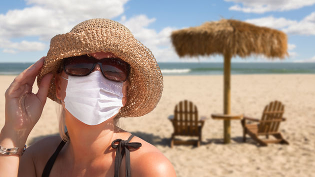 Woman vacationing on a sandy beach wearing a mask.