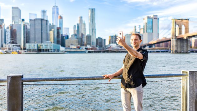 A man poses for a selfie in front of the New York cityscape