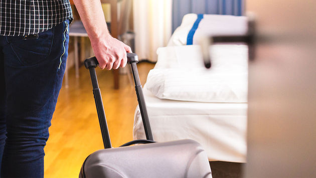 Man pulling suitcase and entering room (Photo via Tero Vesalainen / iStock / Getty Images Plus)