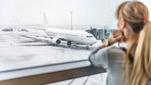 Woman gazing at snowy tarmac and delayed plane flight.