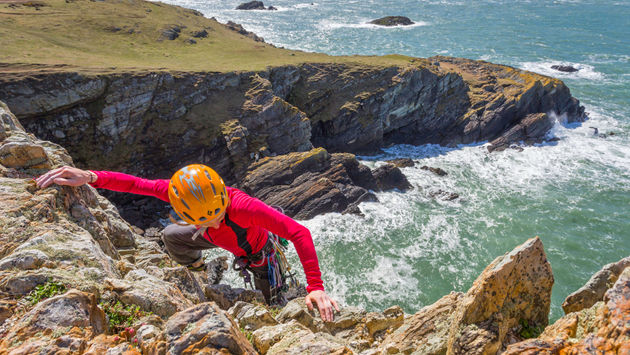 A rock climber reaches the top of a sea cliff at Rhoscolyn, Holy Island.