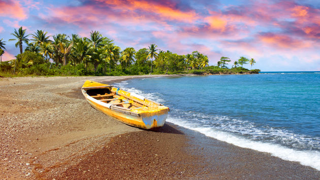 Wooden fishing boat on beach at sunset in Jamaica.