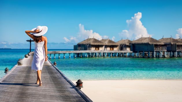 Woman in white walking over a wooden jetty in the Maldives (Photo via SHansche / iStock / Getty Images Plus)