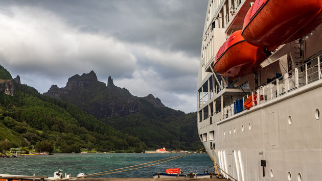 A cruise ship docked at a dock with mountain peaks in the background
