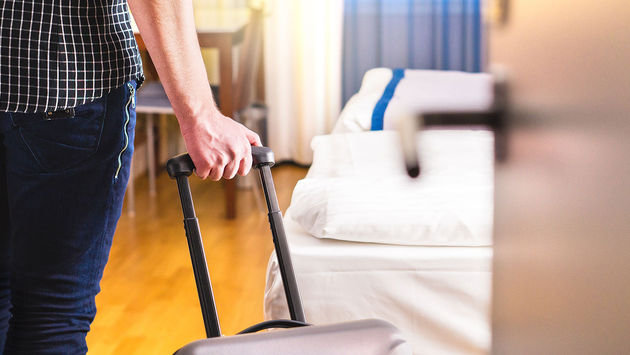 Man pulling suitcase and entering hotel room (Photo via Tero Vesalainen / iStock / Getty Images Plus)