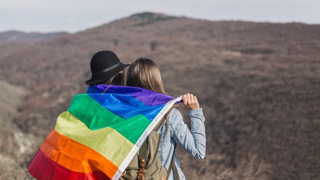 A lesbian couple stands holding the rainbow flag