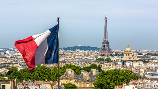 La bandera francesa ondeando con París y la Torre Eiffel de fondo.